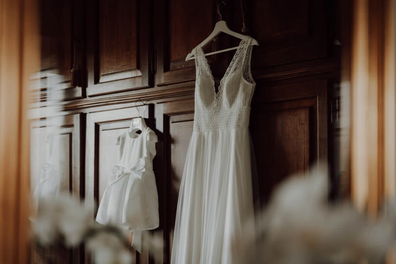 Dettaglio del vestito da sposa assieme al vestito della figlia della sposa, appesi all'armadio di casa, Fotografo di matrimoni in piemonte