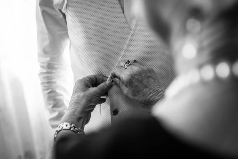 Dettaglio delle mani della madre che abbottona il gilet allo sposo. Fotografo di Matrimoni a Cuneo, Matrimonio a Pianfei